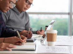 Close-up shot of concentrated Asian students sitting at wooden desk and taking necessary notes while having lecture